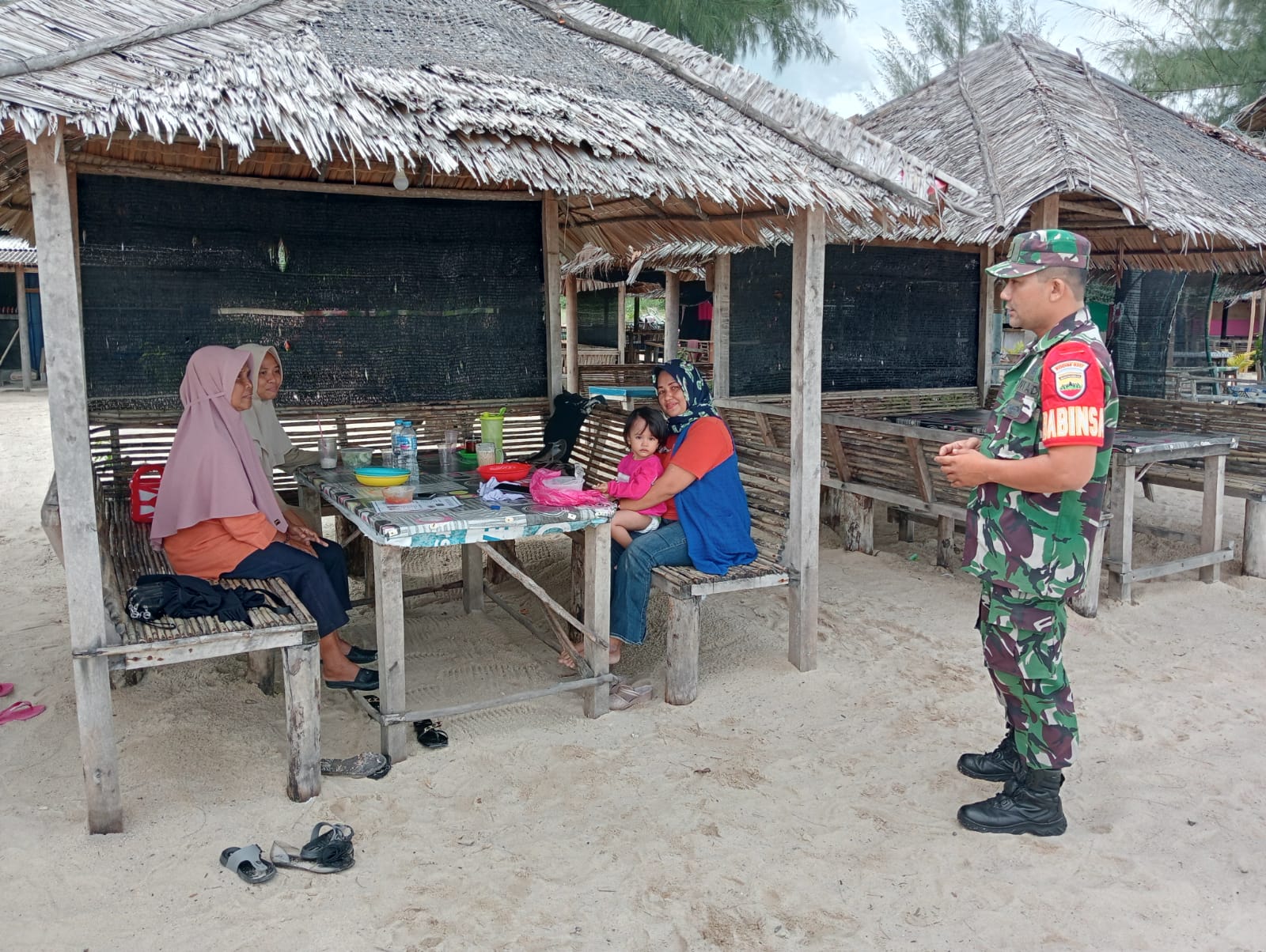 Serda Efin Wijaya dari Babinsa Desa Pongkar, Koramil 04/Tebing, melaksanakan komsos dengan para pengunjung objek wisata Pantai Ketam.